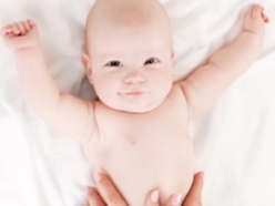 Nahaufnahme eines Babys, das glücklich aussieht und die Arme wegsteckt.